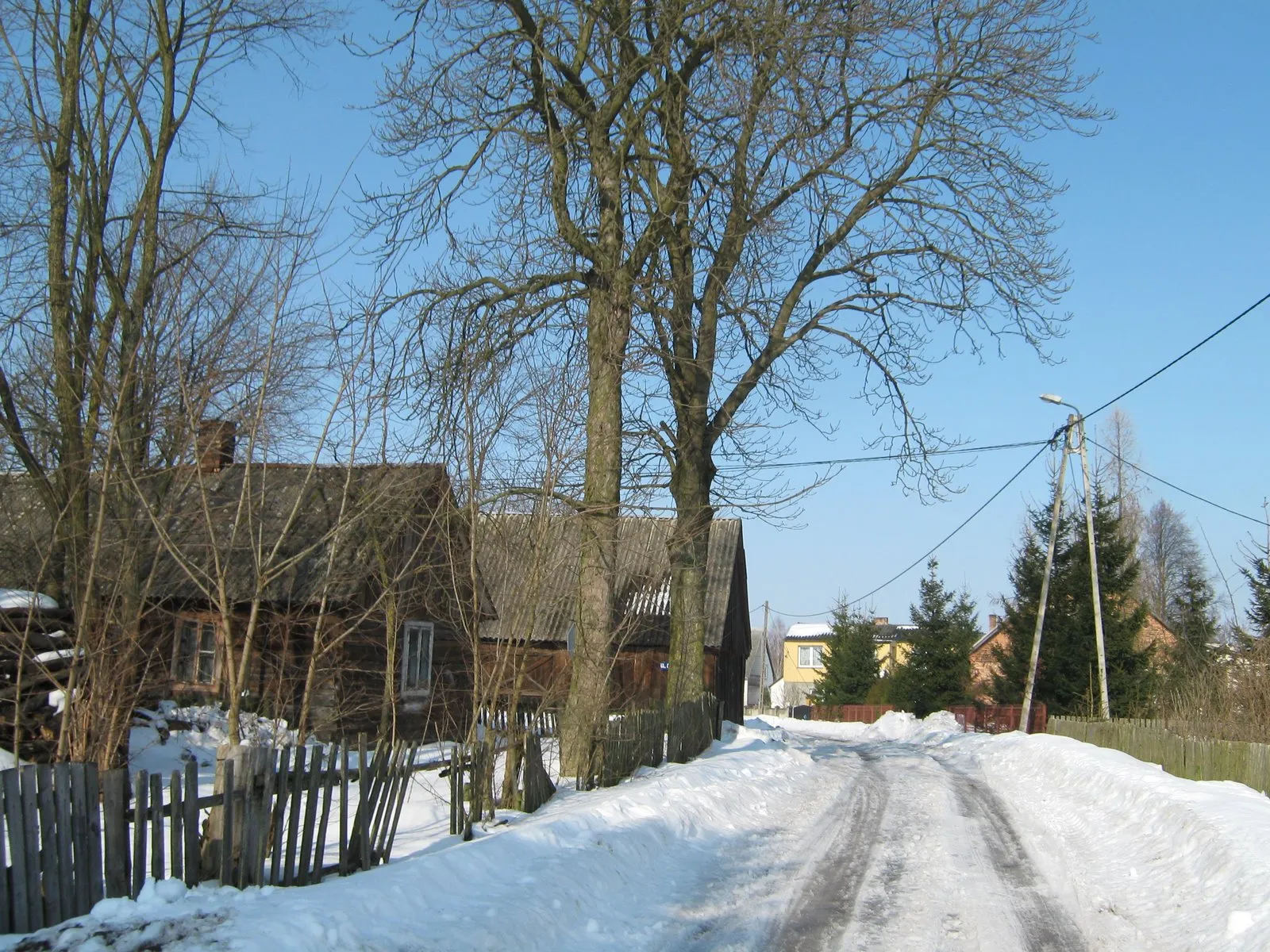 Zaśnieżona ulica we wsi, drewniane domy i płot
